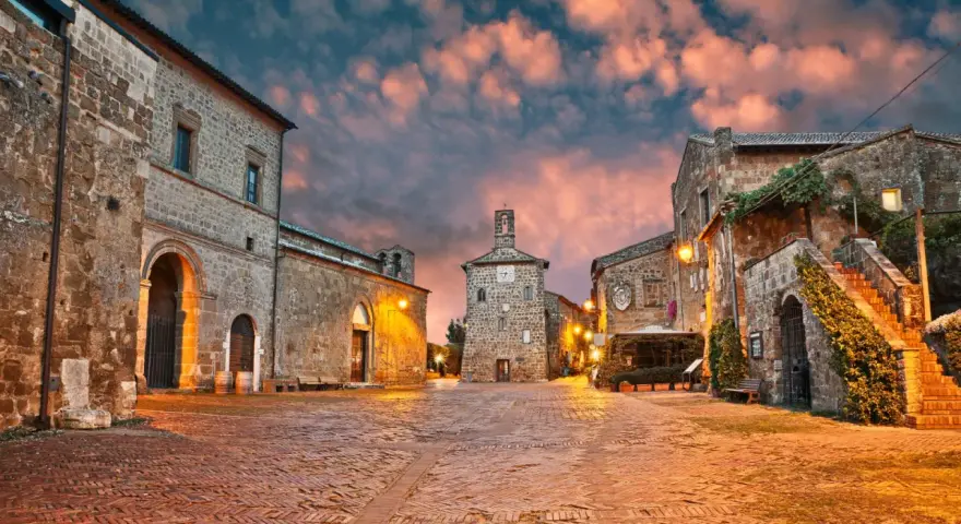 Piazza medievale illuminata al tramonto, con edifici in pietra e un campanile. Un luogo incantevole dove scoprire cosa vedere.