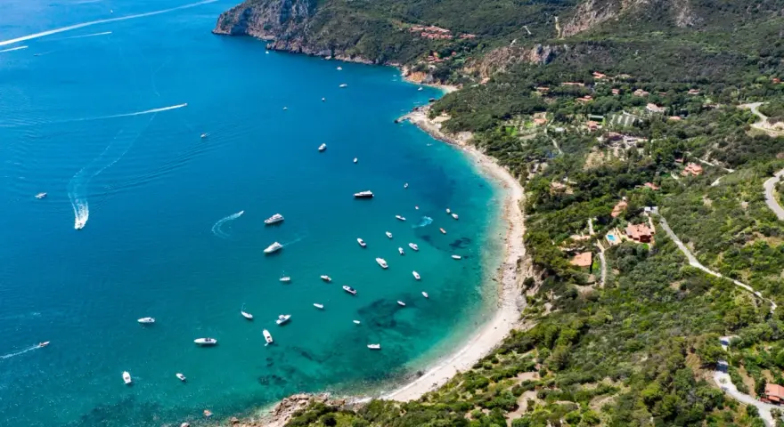 Baia con acque cristalline e numerose barche, incastonata nella costa verdeggiante dell'Argentario, dove si trova un paradiso naturale.