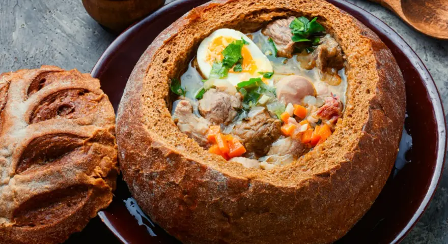 Zuppa polacca servita in una pagnotta scavata, un'ottima idea per cosa mangiare a Cracovia. Carne, uova e verdure in un pane croccante.
