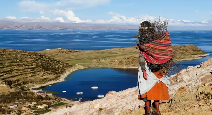 Donna indigena con fascina di legna, vista sul Lago Titicaca, un luogo imperdibile da vedere in Bolivia.