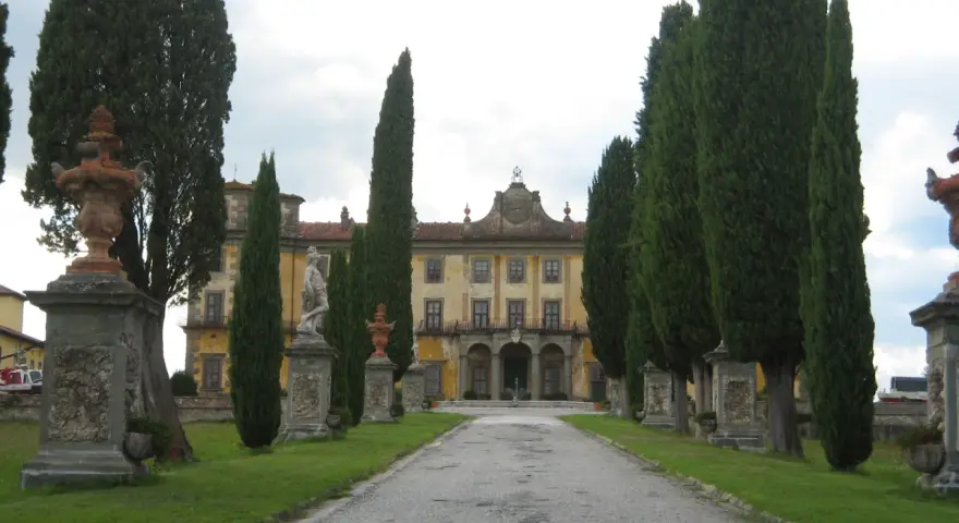 Viale alberato conduce a un palazzo giallo, con statue e fontane, tipico di un borgo a Buggiano.