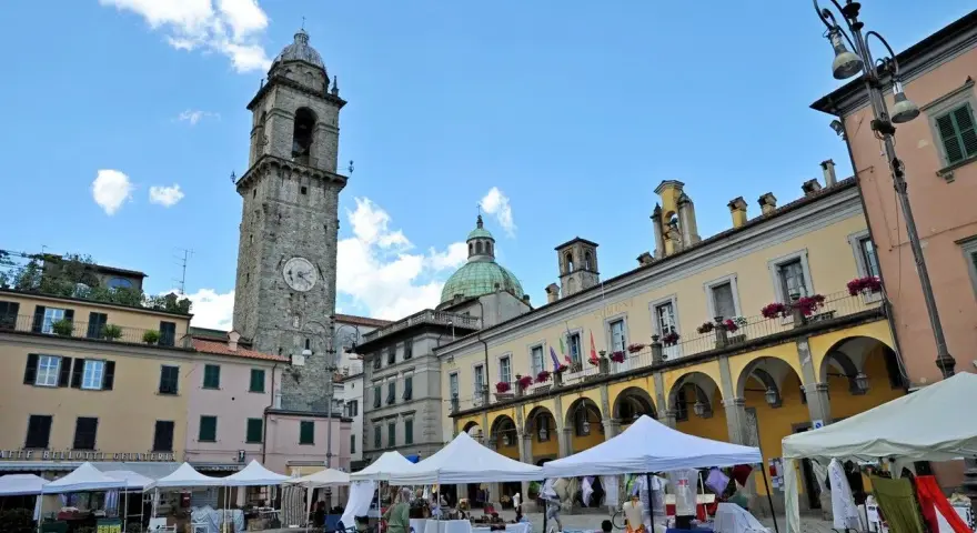 Mercato in piazza a Pontremoli, con la torre civica e il palazzo del Comune. Ecco cosa vedere a Pontremoli: un'atmosfera vivace.
