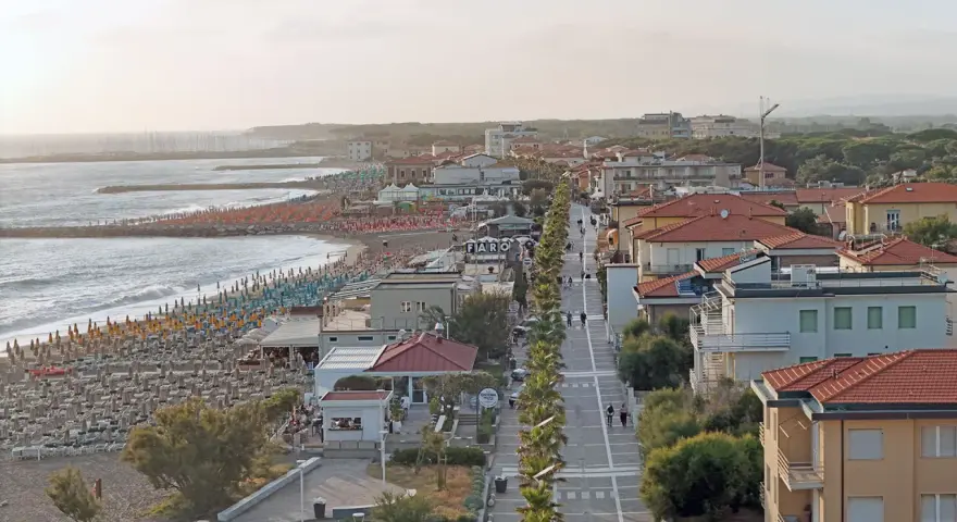 Vista aerea del lungomare di Marina di Cecina con spiaggia attrezzata, mare calmo e case con tetti rossi.