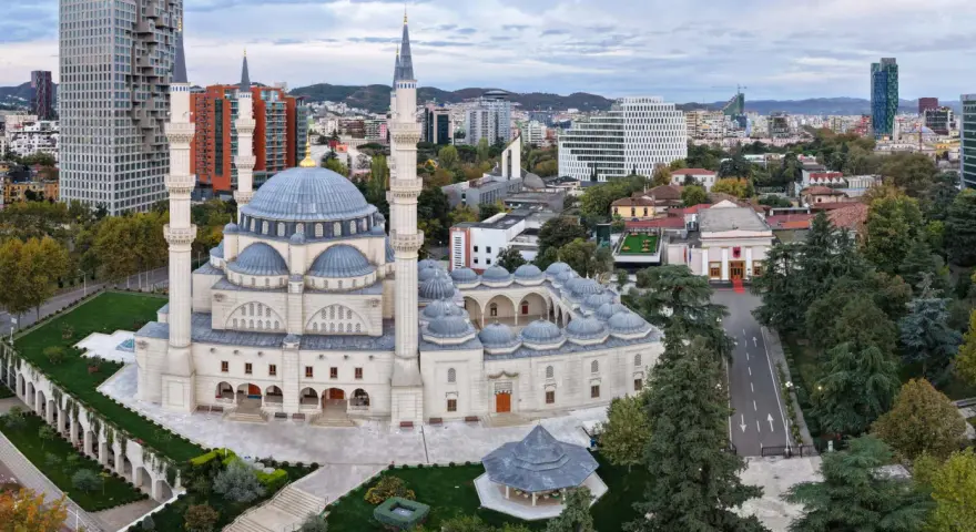 La Grande Moschea e il panorama urbano moderno mostrano dove si trova Tirana, con grattacieli e colline sullo sfondo.
