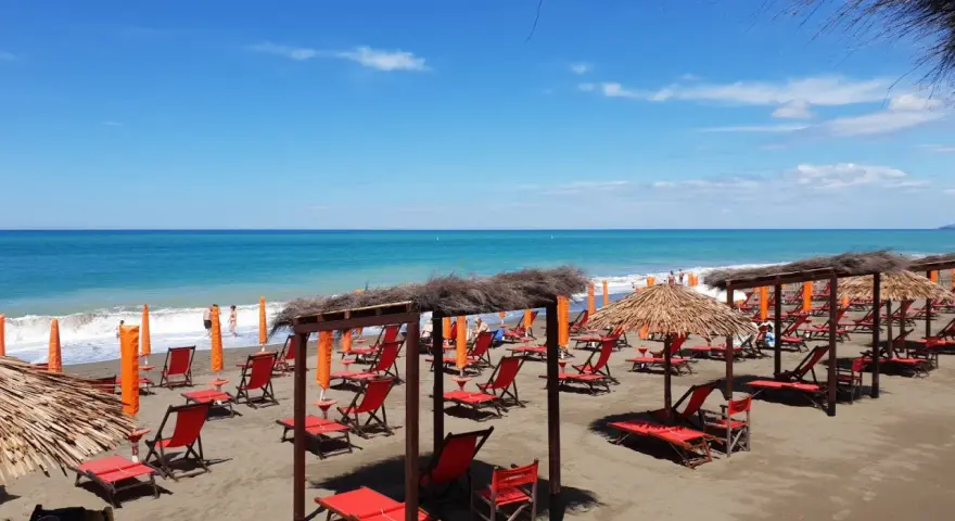 Spiaggia attrezzata a Marina di Bibbona con lettini rossi, ombrelloni di paglia e il mare azzurro sullo sfondo.
