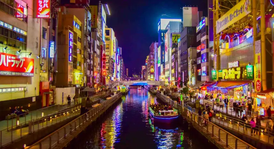 Un canale illuminato da insegne al neon a Osaka, cosa vedere: un tour in battello tra edifici vibranti e riflessi sull'acqua.