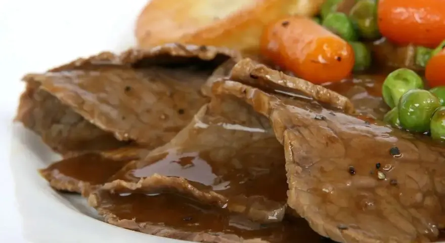 Fette di arrosto con sugo, piselli, carote e patate arrosto, un classico tra i piatti tipici del Regno Unito.