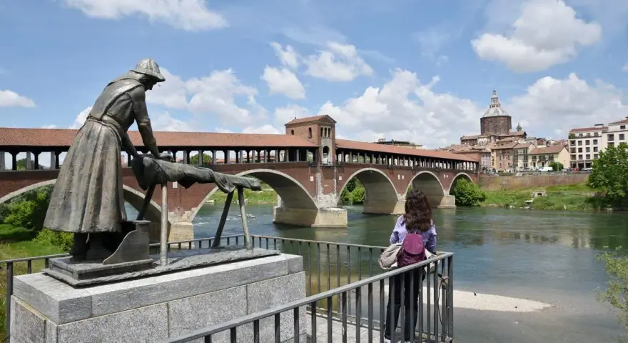 Pavia cosa vedere in un giorno: il Ponte Coperto con la statua della lavandaia e la cupola del Duomo sullo sfondo.