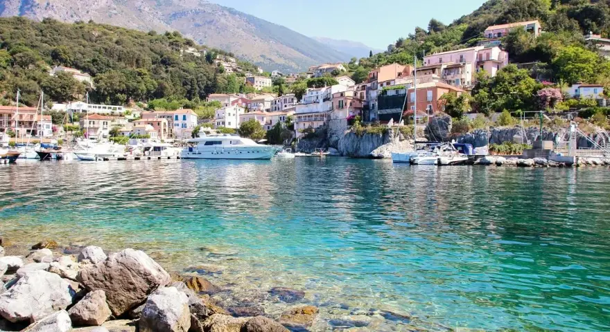 Un borgo colorato su una collina, con barche e yacht in un mare cristallino. Un esempio di posti belli da visitare in Italia a poco prezzo.