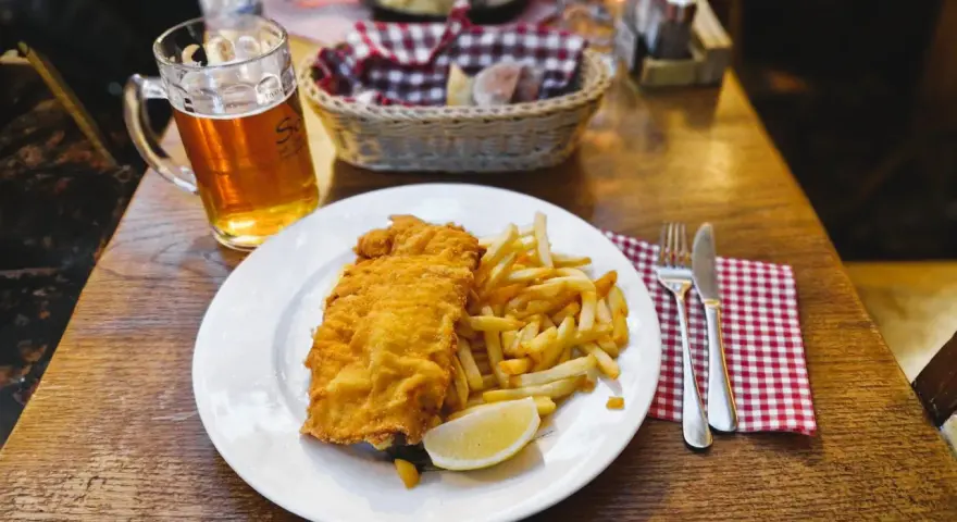 Piatto di pesce fritto e patatine fritte, con una birra chiara, un classico per scoprire cosa mangiare a Lubiana.