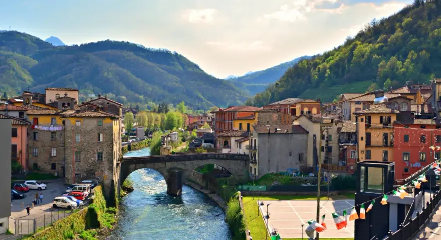 Un pittoresco scorcio di Castelnuovo di Garfagnana con il fiume Serchio che attraversa il borgo, circondato da colline verdi.