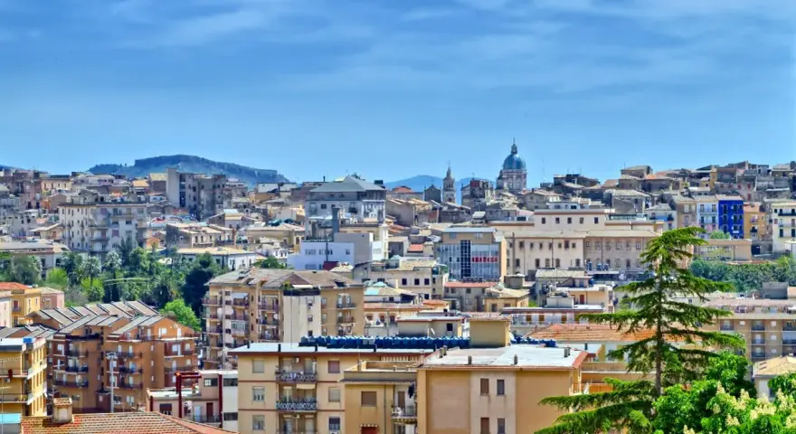 Panoramica di **Caltanissetta cosa vedere**: tetti rossi, palazzi colorati e la cupola di una chiesa sotto un cielo azzurro.