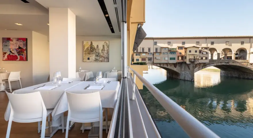 Tavoli apparecchiati in un ristorante con vista su Ponte Vecchio. Un'ottima opzione per sapere dove mangiare a Firenze.