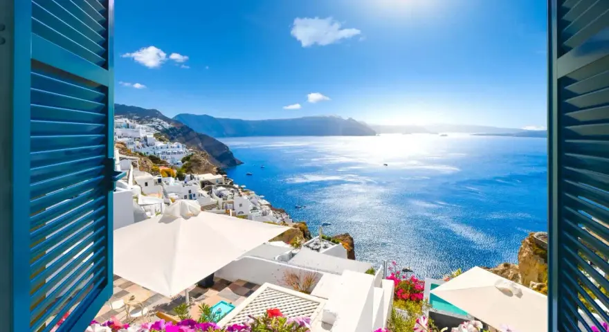 Vista mozzafiato su Santorini, perfetta per sapere dove andare in vacanza a giugno. Case bianche a picco sul mare blu intenso, fiori colorati e sole splendente.