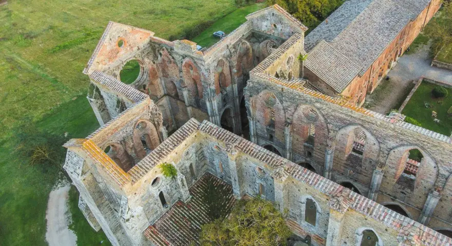 Rovine suggestive dell'abbazia nel Val di Merse, con archi gotici e tetti in tegole rosse, immerse nel verde della campagna toscana.