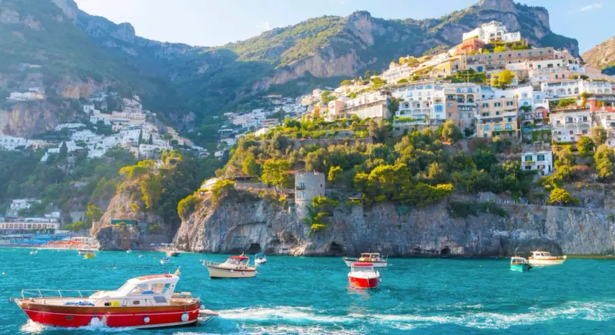 Barche a vela solcano le acque turchesi, con case colorate aggrappate alle scogliere dei paesi della costiera amalfitana.