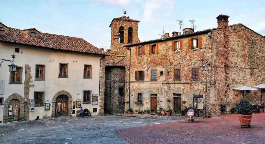 Piazza di un borgo toscano, ideale tra i borghi da visitare in 2 giorni. Edifici in pietra e mattoni, campanile e scorci suggestivi.