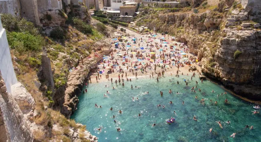 Spiaggia affollata e mare cristallino a Polignano a Mare. Ecco cosa fare: godersi il sole, nuotare e rilassarsi tra le scogliere.