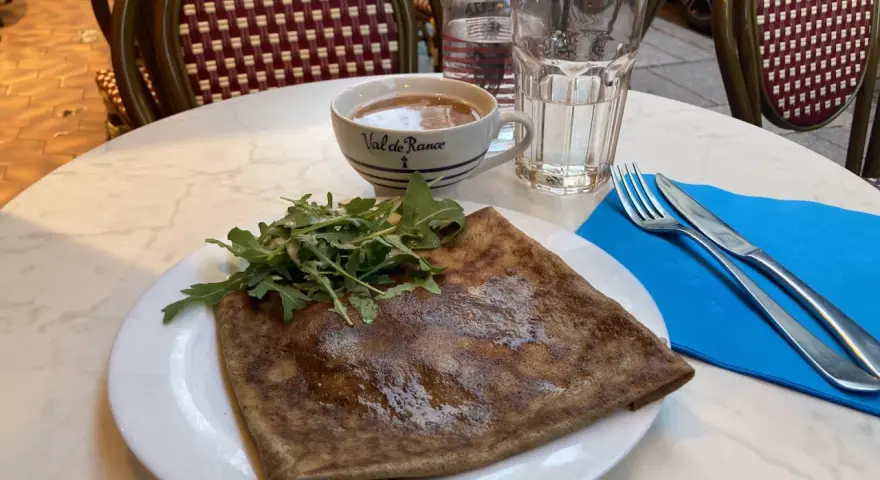 Crepe salata con rucola, una tazza di caffè e un bicchiere d'acqua, un assaggio dei piatti tipici parigini.