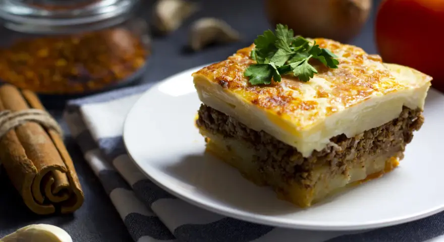 Un assaggio di cosa mangiare ad Atene: moussaka fatta in casa, con strati di patate, carne macinata e besciamella dorata, guarnita con prezzemolo fresco.