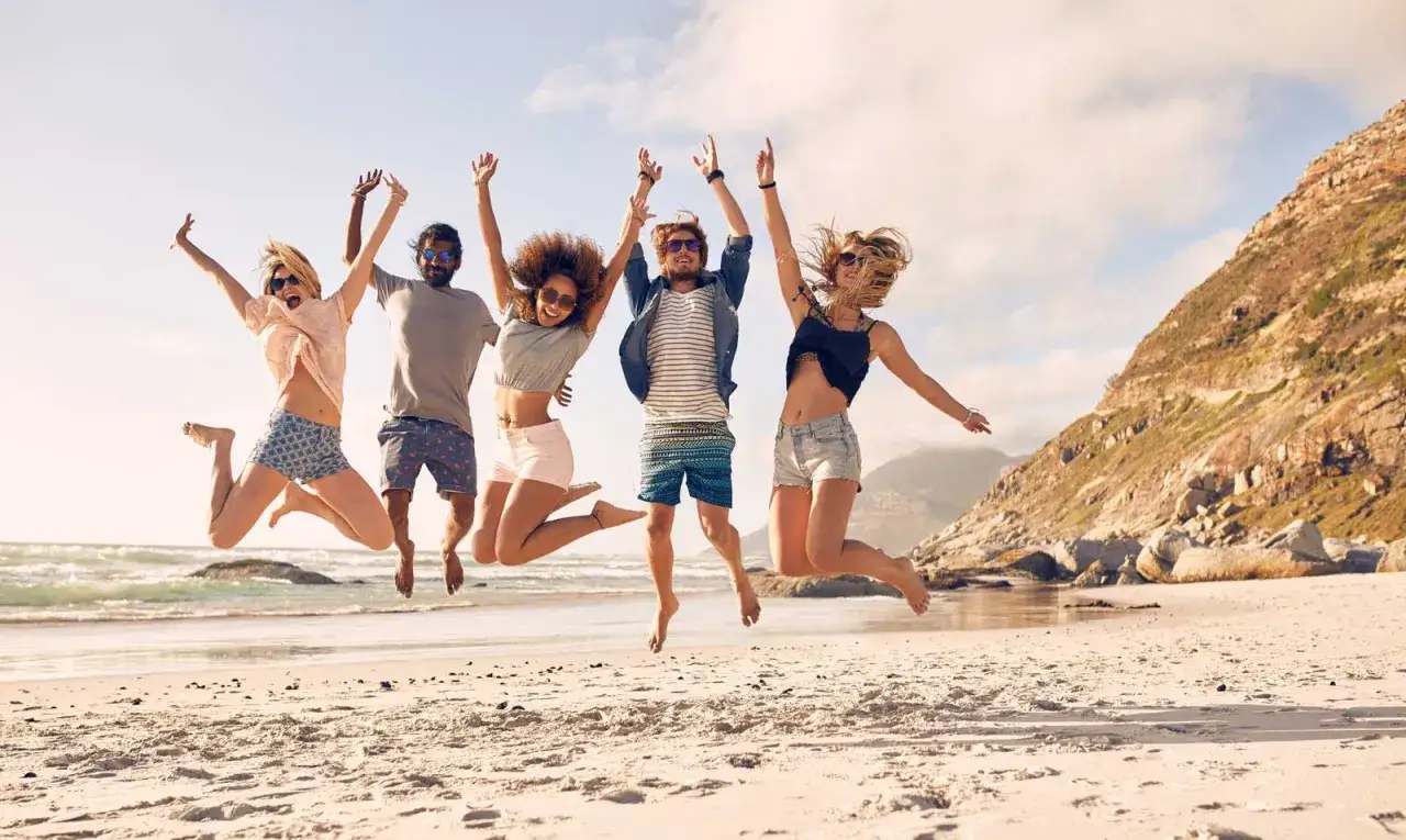 Cinque giovani saltano felici su una spiaggia dorata, perfette mete estive per ragazzi in cerca di divertimento e avventura.