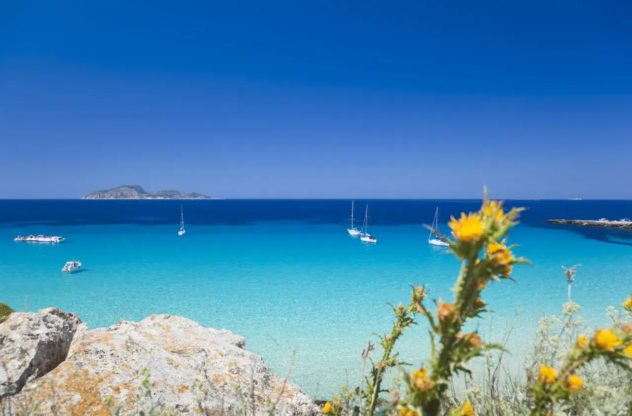 Viste mozzafiato delle spiagge Sicilia orientale, con acque cristalline, barche a vela e un'isola all'orizzonte.
