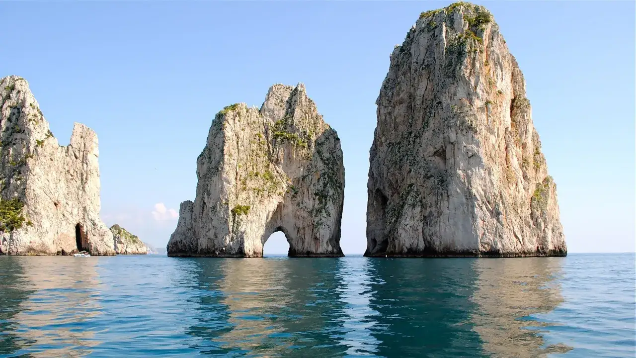 Faraglioni dell'isola di Capri, imponenti rocce che emergono dal mare blu, con un arco naturale scavato nella roccia.