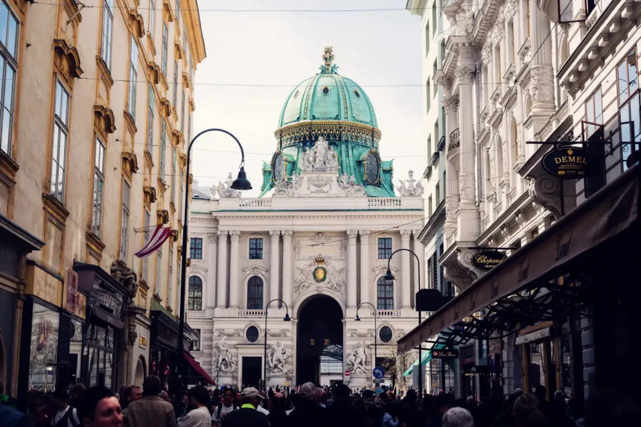 Una giornata a Vienna: la maestosa cupola verde del palazzo imperiale domina la scena, tra eleganti palazzi e negozi storici.