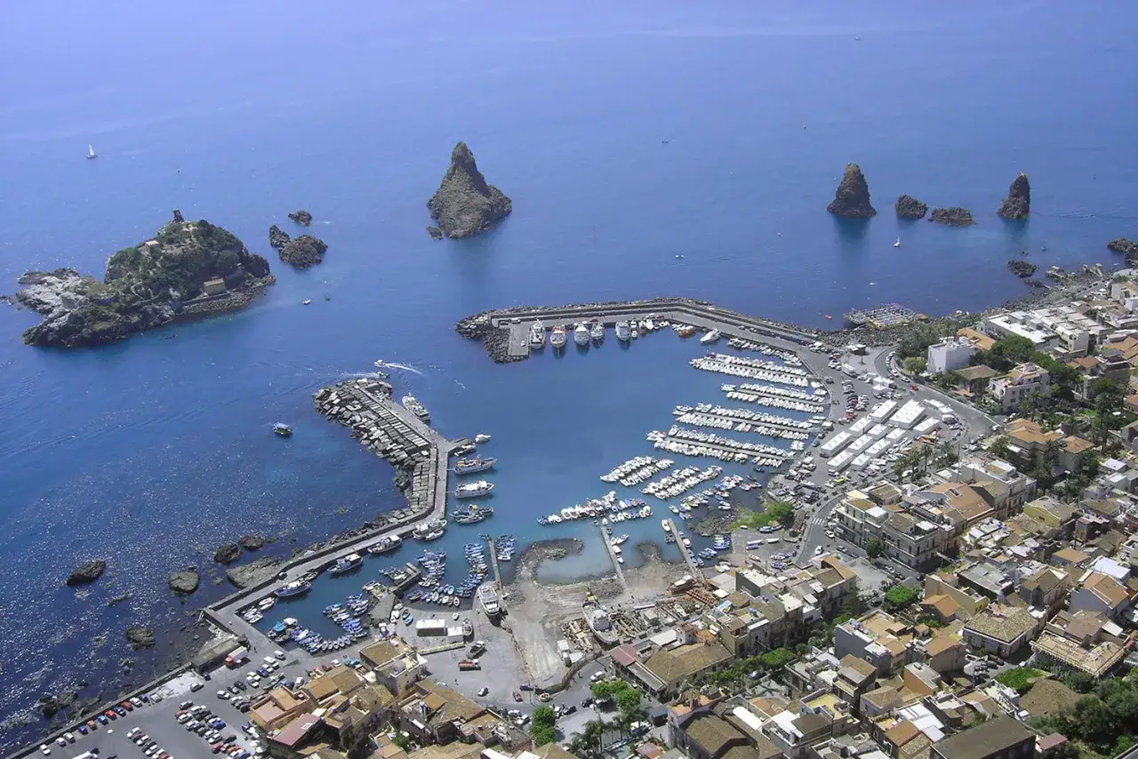 Acitrezza cosa vedere: vista aerea del porto con barche, faraglioni e case sul mare.