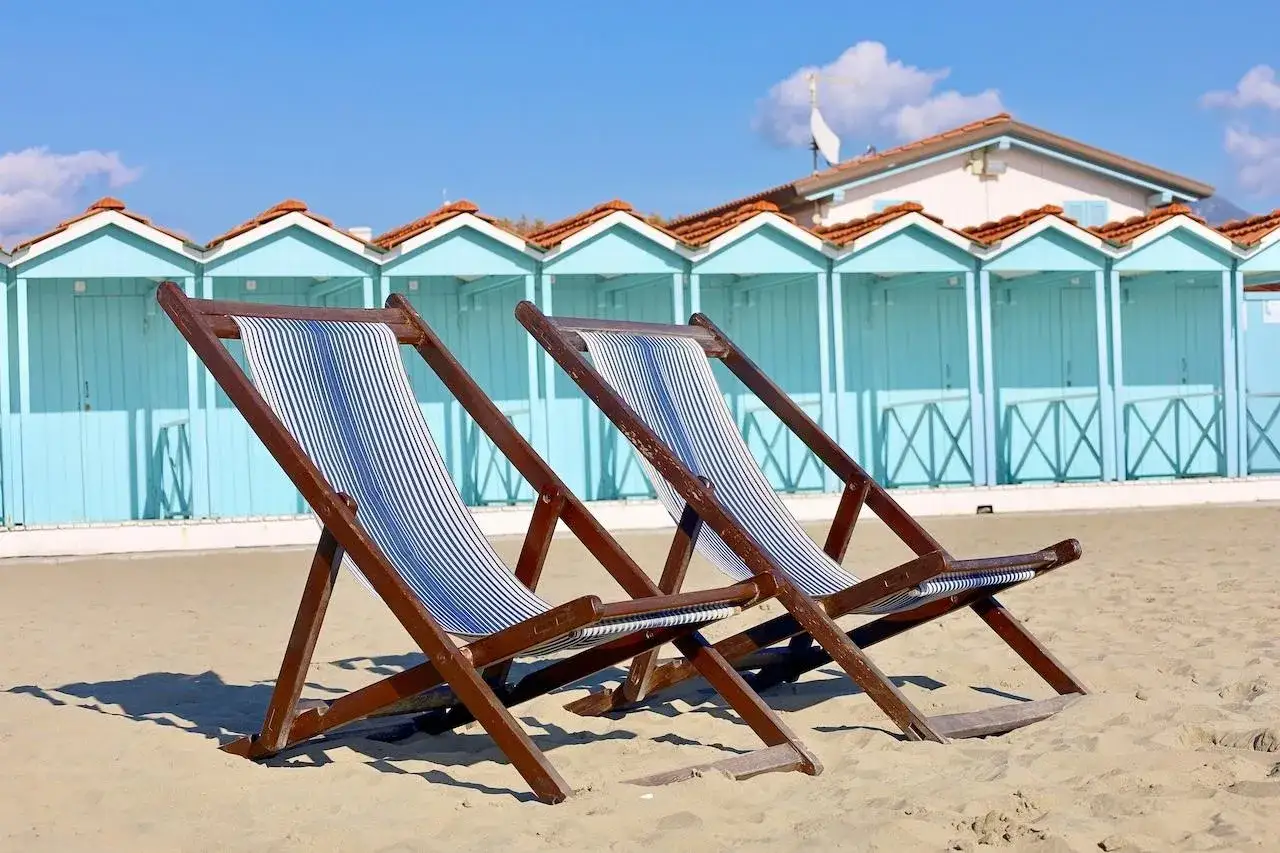 Due sdraio a righe blu e bianche sulla sabbia di Forte dei Marmi, con cabine azzurre sullo sfondo.