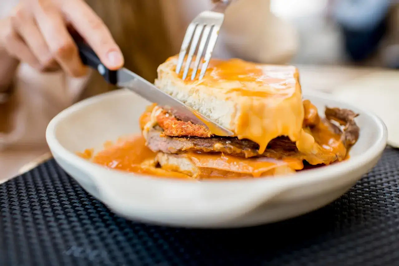 Un assaggio di cosa mangiare a Porto: una francesinha, un panino ricco con carne, formaggio fuso e salsa piccante, pronto per essere gustato.