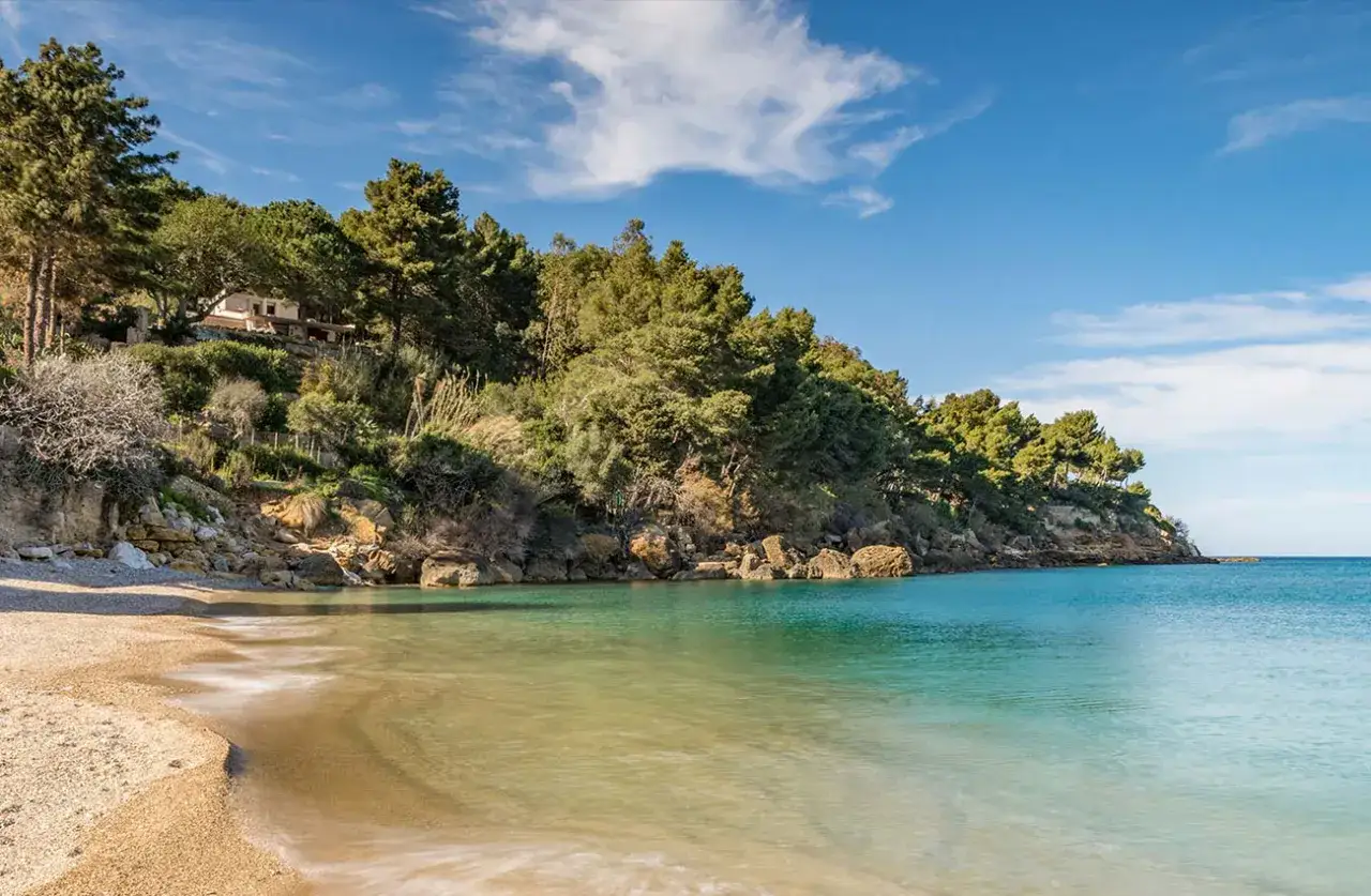Spiaggia tranquilla con acque cristalline e una villa immersa nel verde sulla costa di Castellammare del Golfo.