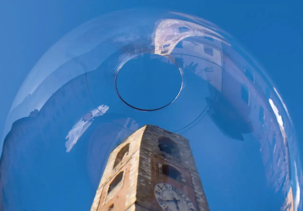 Torre dell'orologio di Colle Val d'Elsa riflessa in una bolla di sapone, con il cielo azzurro sullo sfondo.