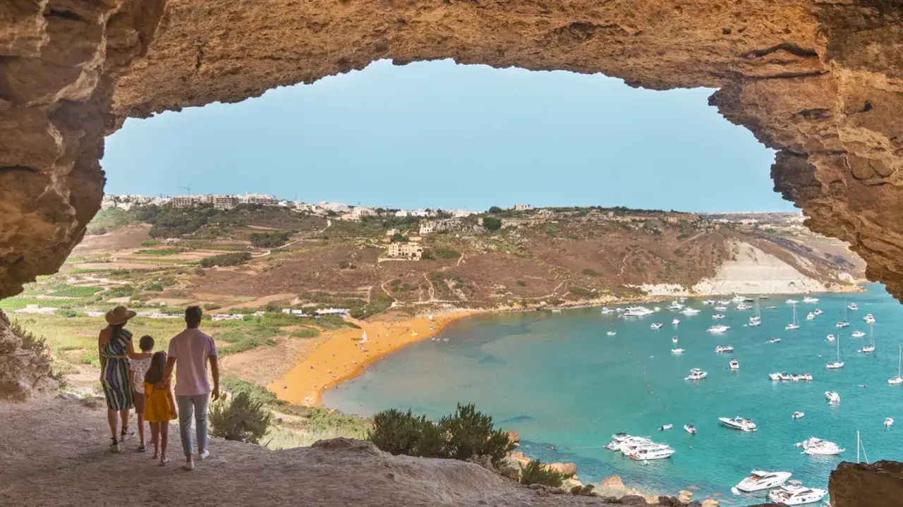 Famiglia ammira la baia di Ramla, un luogo perfetto per scoprire cosa fare a Malta, con la sua spiaggia dorata e le barche nel mare turchese.