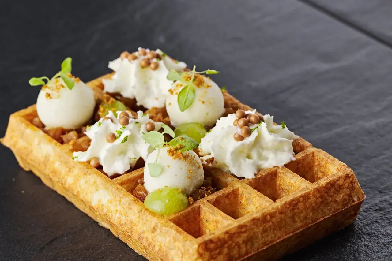 Un waffle belga con gelato, panna montata e uva. Un'idea golosa su cosa mangiare a Bruxelles per un dolce indimenticabile.