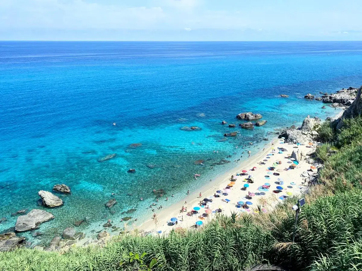 Spiaggia affollata con ombrelloni colorati e gente che nuota nel mare bello Italia. Acqua cristallina e scogli.