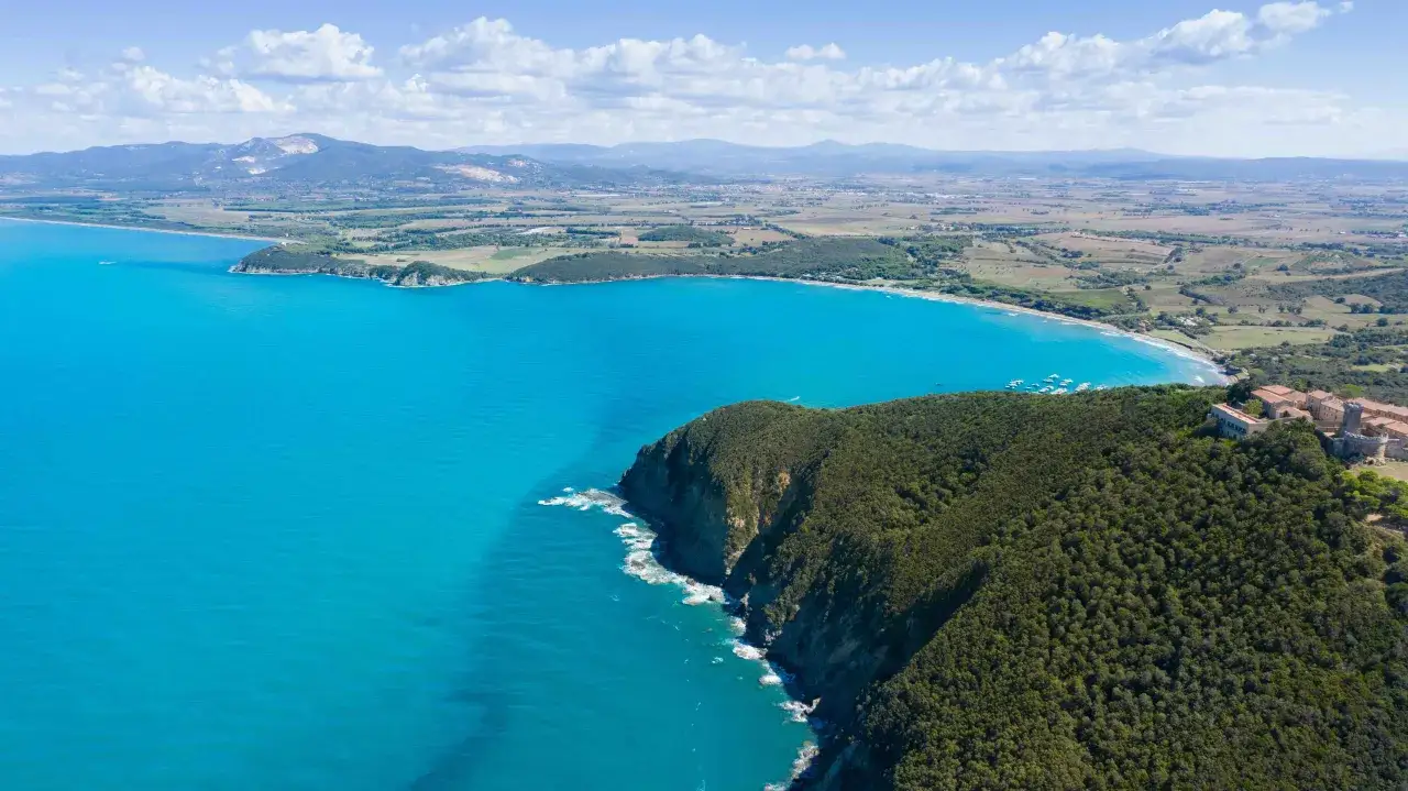 Vista aerea della costa toscana con il mare azzurro e la vegetazione lussureggiante che scende verso la spiaggia di Marina di Bibbona.