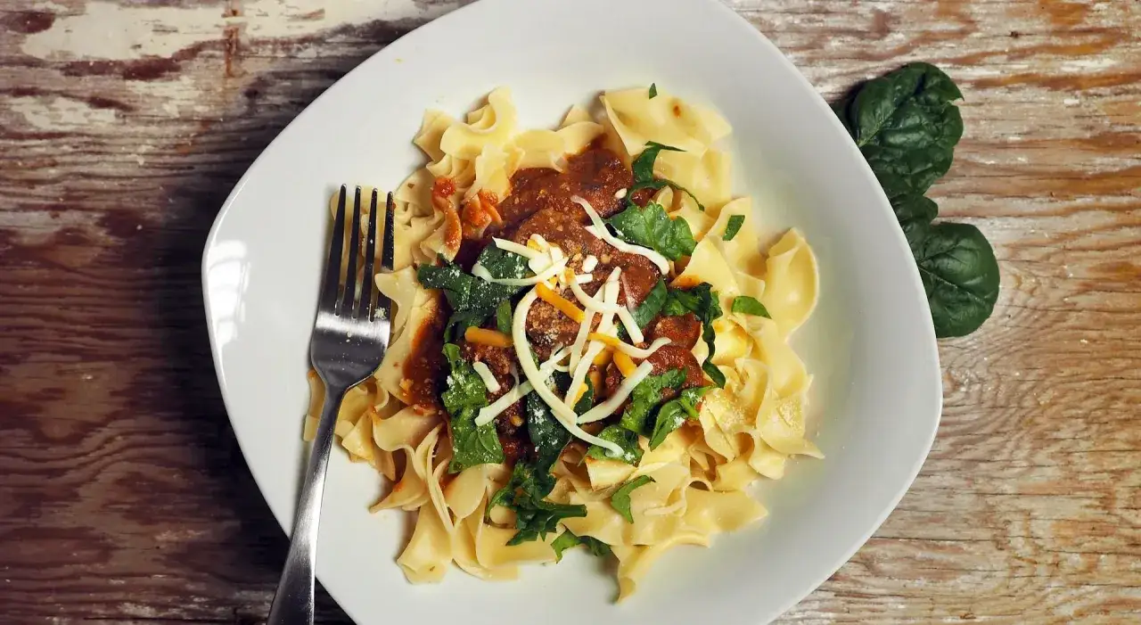 Un piatto di pasta fresca con ragù, spinaci e formaggio grattugiato, un assaggio dei piatti tipici Matera.
