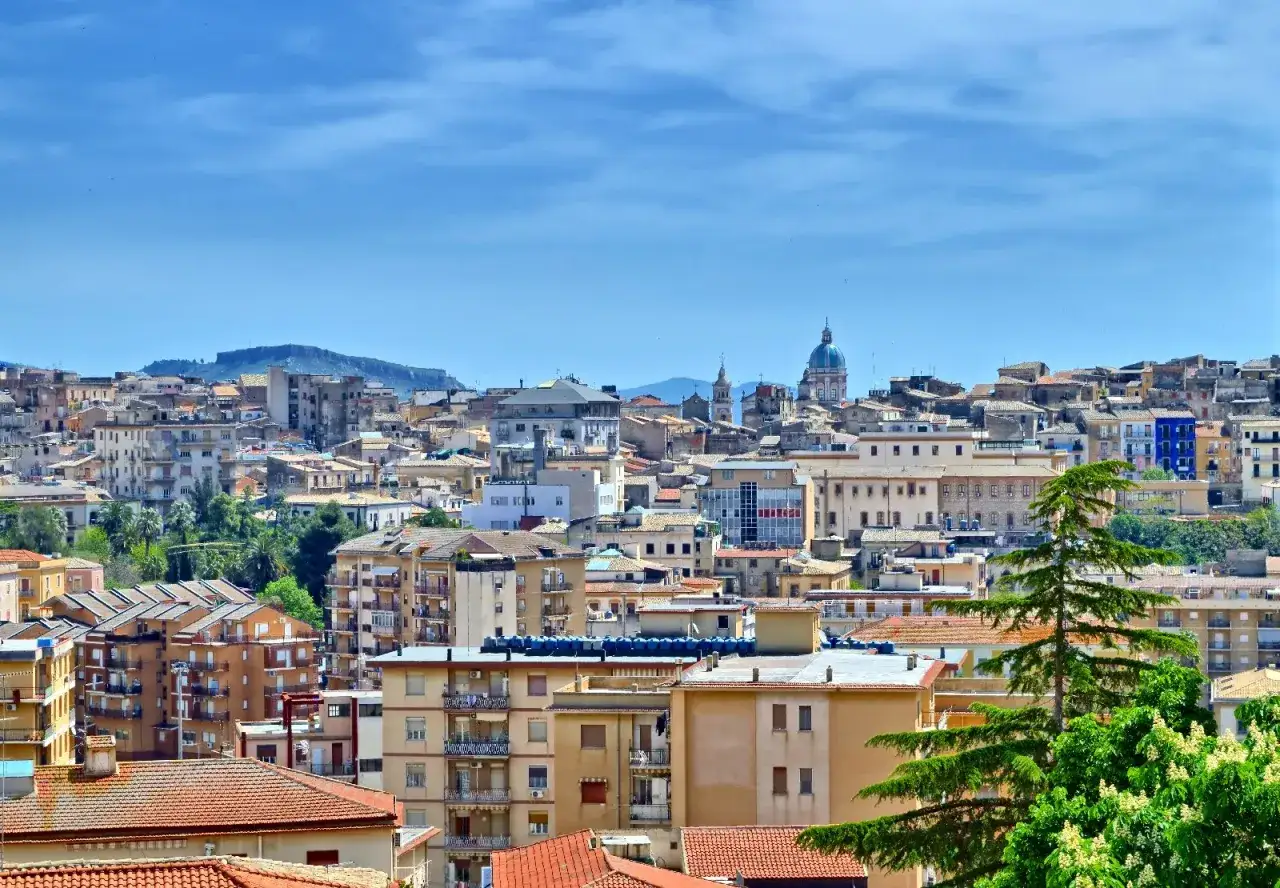 Panoramica di Caltanissetta cosa vedere: tetti rossi, palazzi colorati e la cupola di una chiesa sotto un cielo azzurro.