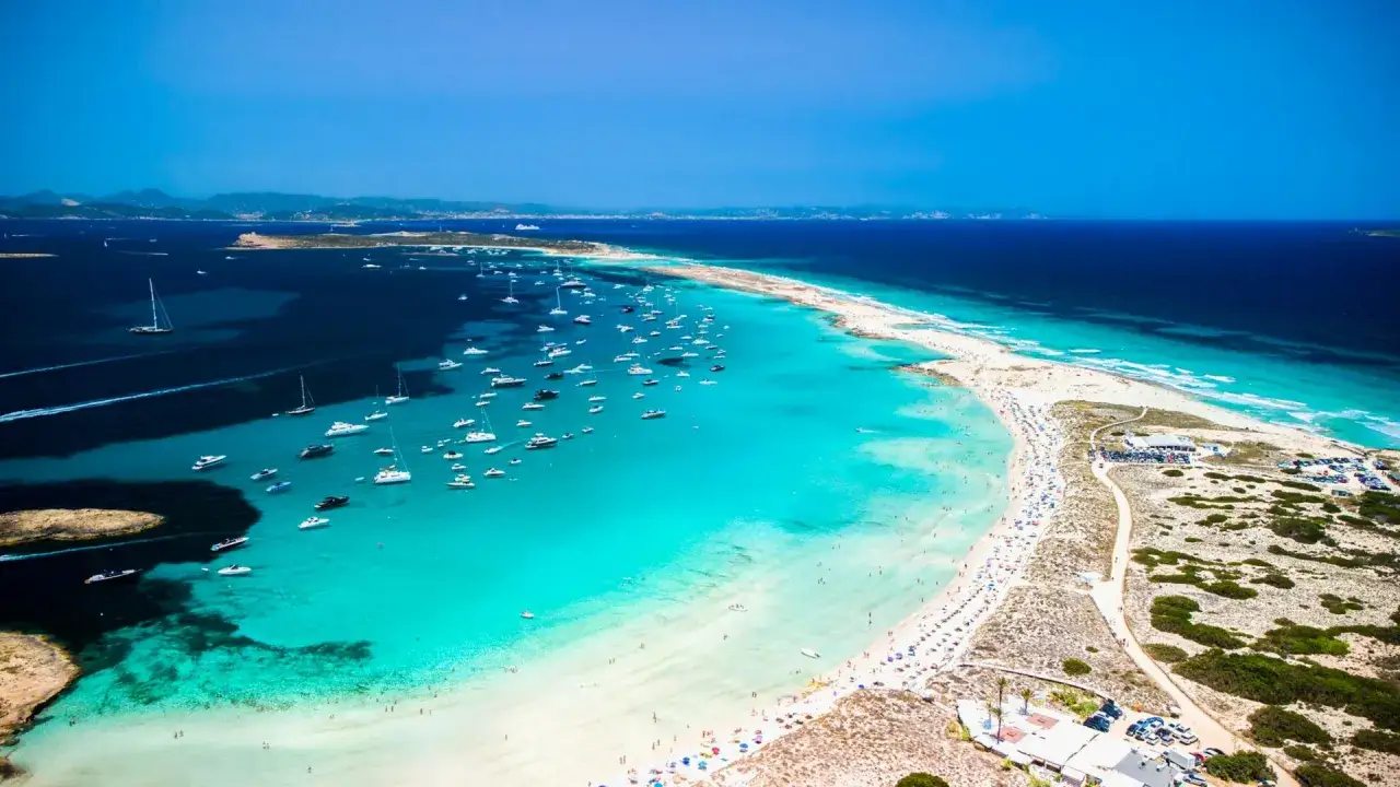 Spiaggia paradisiaca in Spagna dove andare al mare, con acque turchesi, sabbia bianca e centinaia di barche.