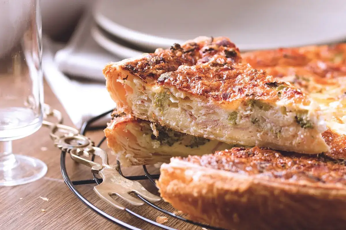 Fetta di quiche, uno dei piatti tipici di Parigi, con broccoli e prosciutto, su una griglia.