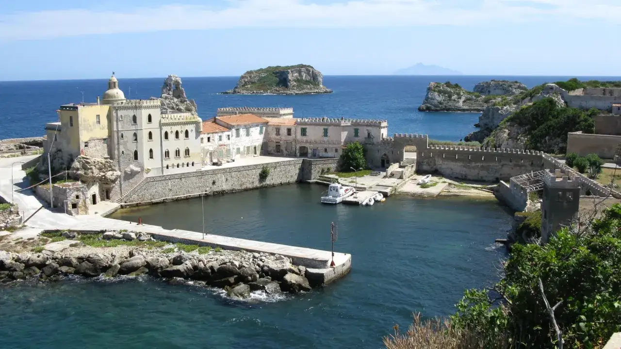 Antico porto dell'isola di Pianosa, con edifici storici, mura fortificate e il mare azzurro.