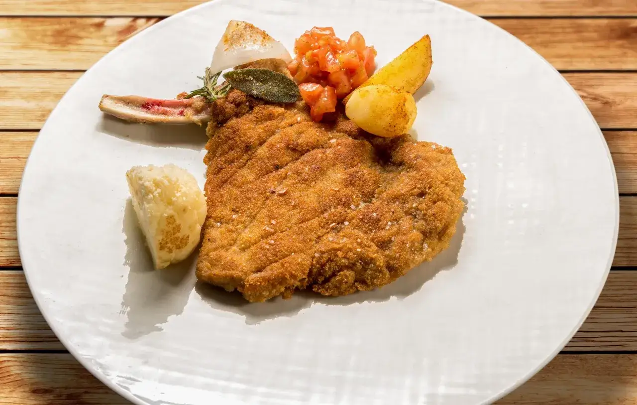 Cotoletta alla milanese croccante con patate e pomodoro. Un classico da provare se ti chiedi cosa mangiare a Milano.
