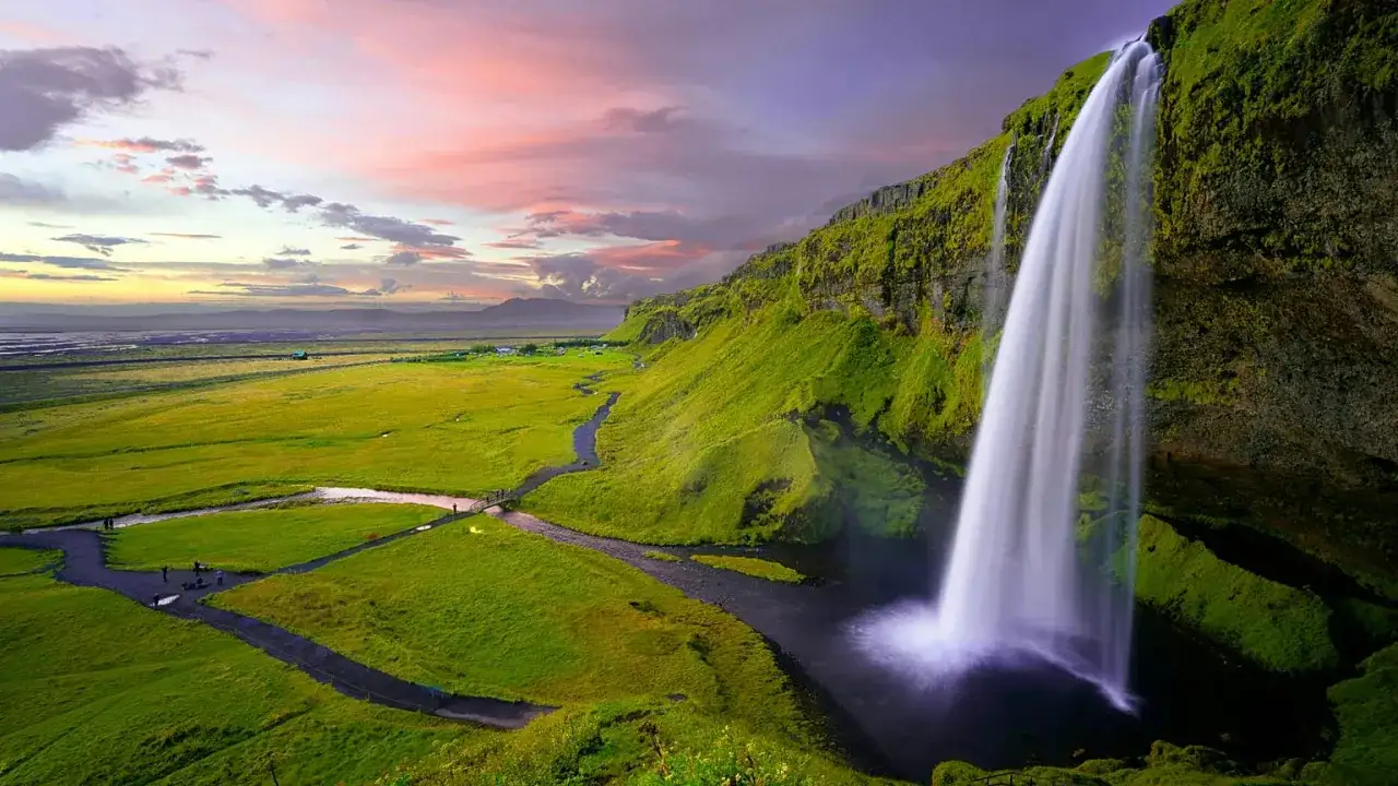 Cascata imponente in un paesaggio verdeggiante, con un cielo rosa al tramonto. Un luogo che evoca la pace e la bellezza dei paesi più sicuri al mondo.