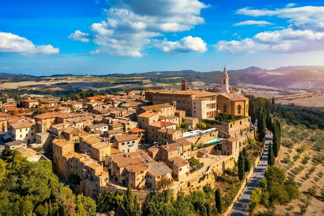 Borghi medievali del Val d'Orcia, con tetti in cotto e colline ondulate sotto un cielo azzurro.