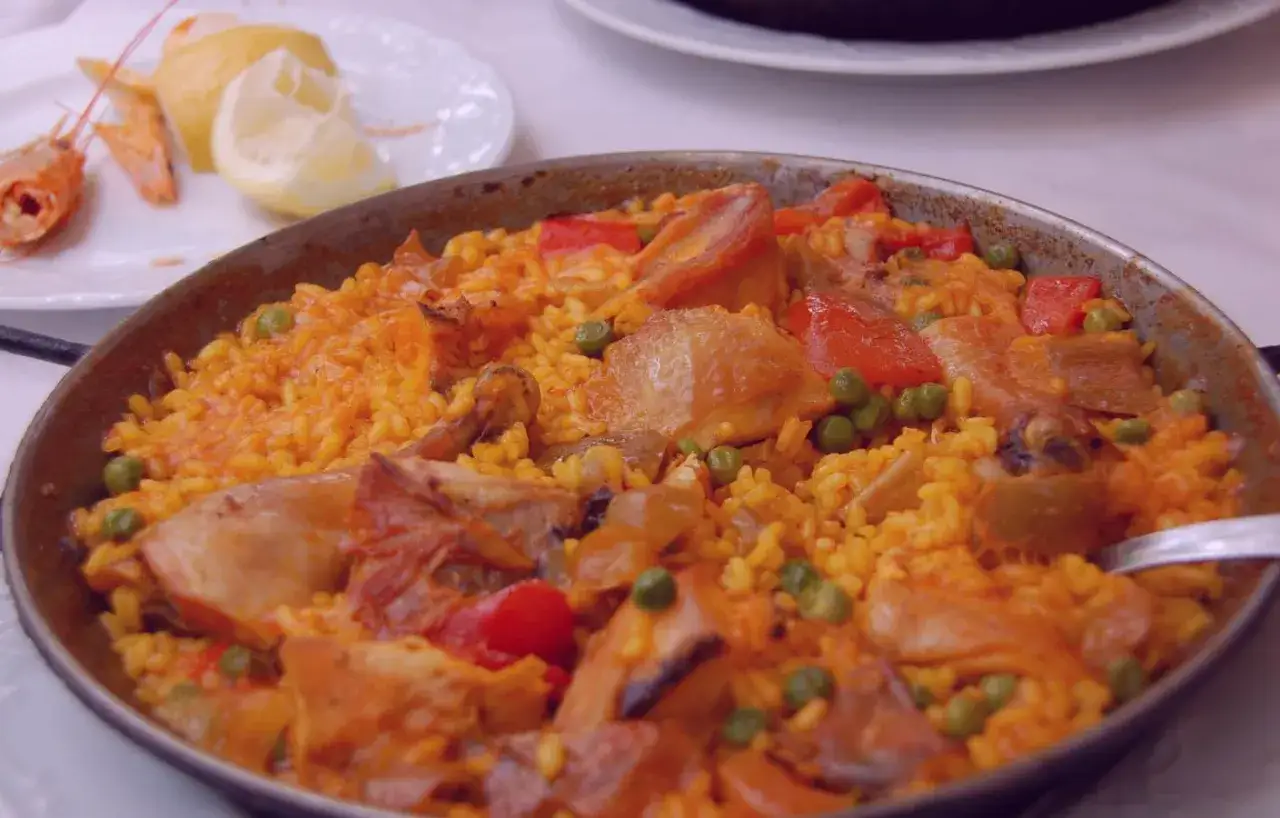 Paella di pollo e verdure, uno dei piatti tipici di Madrid, servita in una padella con limone e gamberi a lato.
