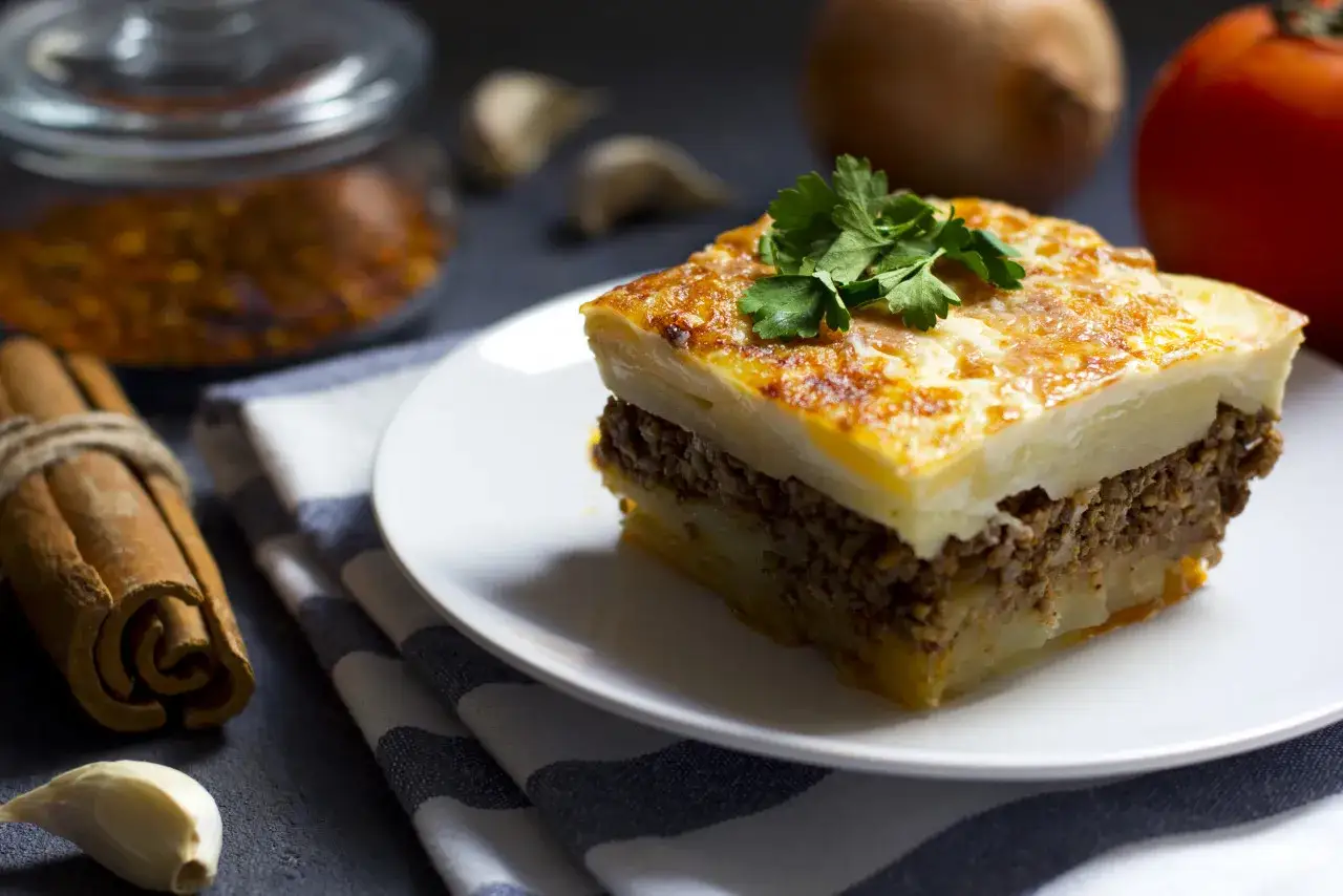 Un assaggio di cosa mangiare ad Atene: moussaka fatta in casa, con strati di patate, carne macinata e besciamella dorata, guarnita con prezzemolo fresco.
