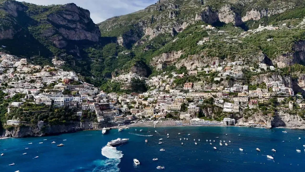 Case colorate aggrappate alla scogliera, un gioiello tra i paesi della costiera amalfitana, con barche che solcano il mare blu.