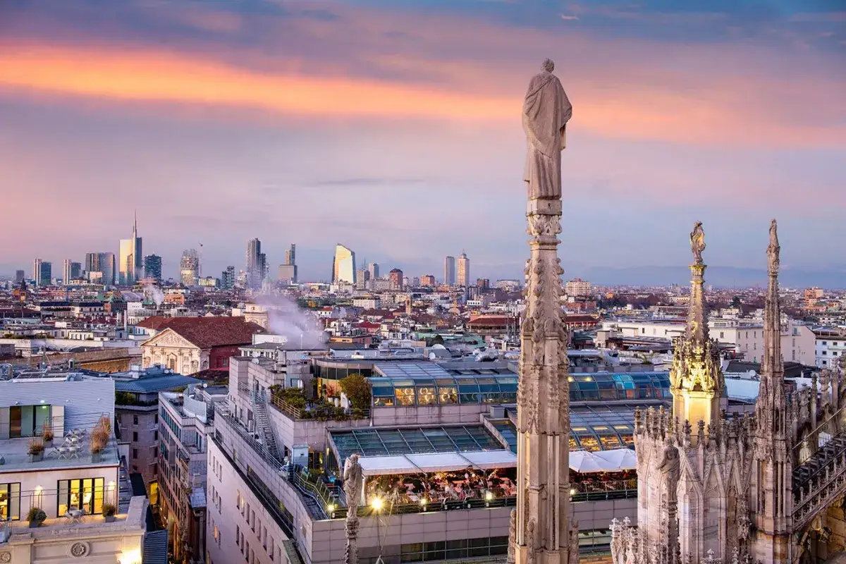 Panoramica di Milano al tramonto, una delle più belle città da visitare nel nord Italia. Grattacieli moderni e guglie gotiche si stagliano contro un cielo colorato.