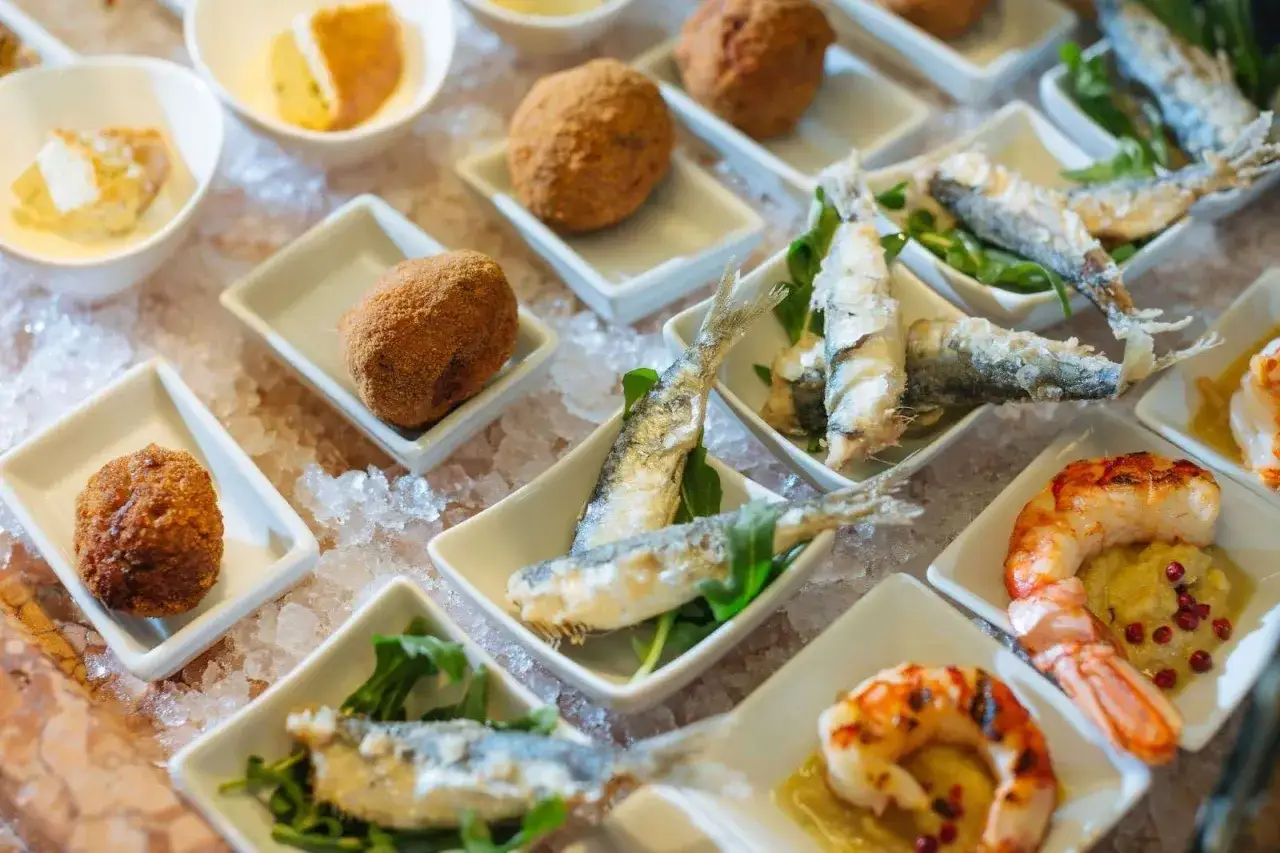 Assaggio di piatti tipici veneziani: crocchette dorate, sarde fritte e gamberi grigliati, serviti su un letto di ghiaccio.